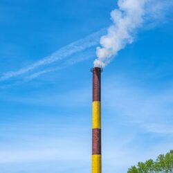 Industrial,Smokestack,Emitting,Smoke,Against,Blue,Sky.,The,Image,Captures