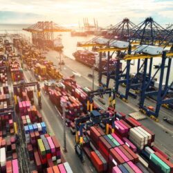 Container,Ship,Docked,At,Port,With,Cargo,Trucks,And,Cranes.