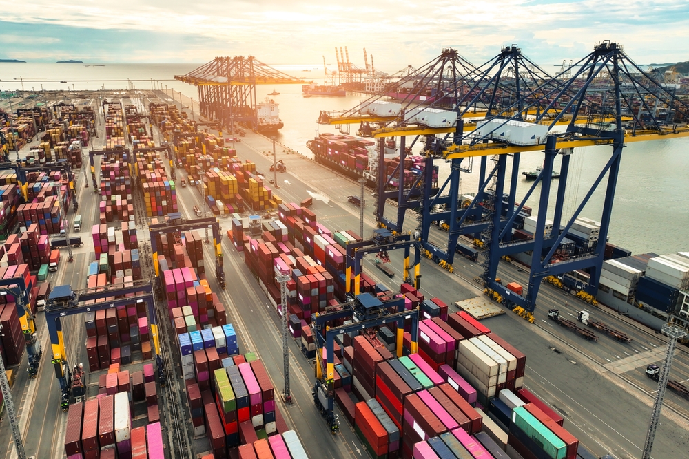 Container,Ship,Docked,At,Port,With,Cargo,Trucks,And,Cranes.